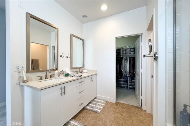 bathroom featuring a walk in closet, double vanity, a shower with shower door, and a sink