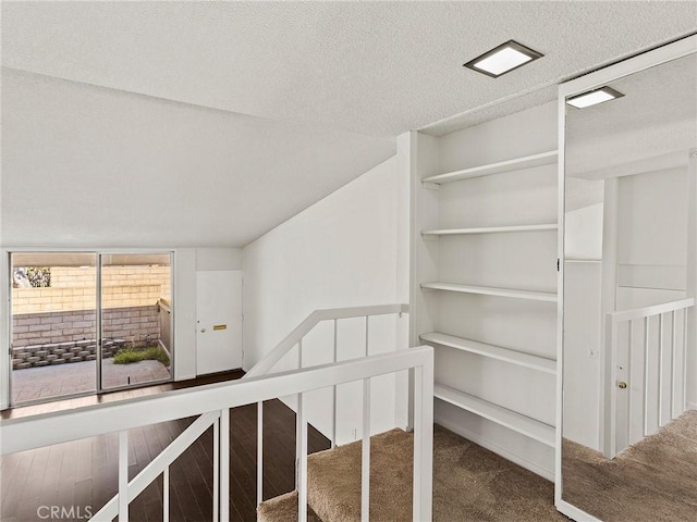 stairway featuring lofted ceiling, carpet floors, and a textured ceiling