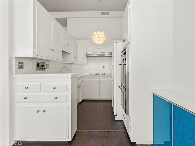 kitchen featuring visible vents, backsplash, under cabinet range hood, dark wood finished floors, and white cabinets