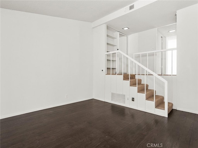 unfurnished room with visible vents, baseboards, wood finished floors, and stairway