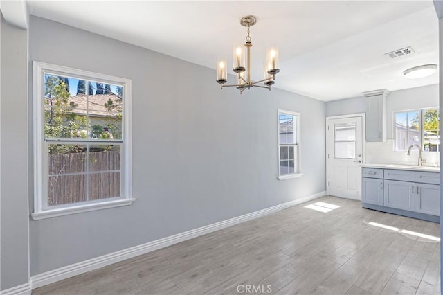 unfurnished dining area with visible vents, baseboards, a chandelier, light wood-style flooring, and a sink