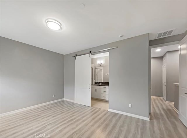 unfurnished bedroom with light wood finished floors, visible vents, baseboards, and a barn door