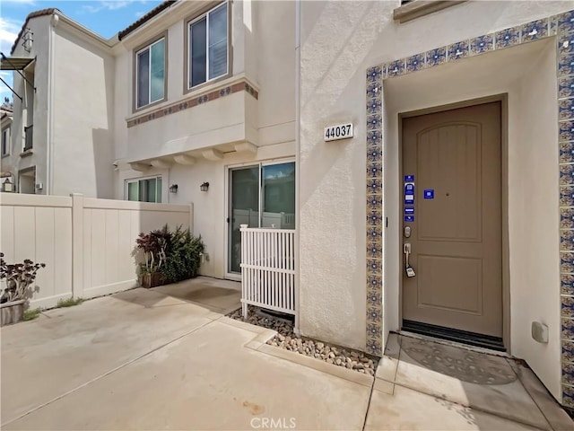 view of exterior entry featuring stucco siding and fence