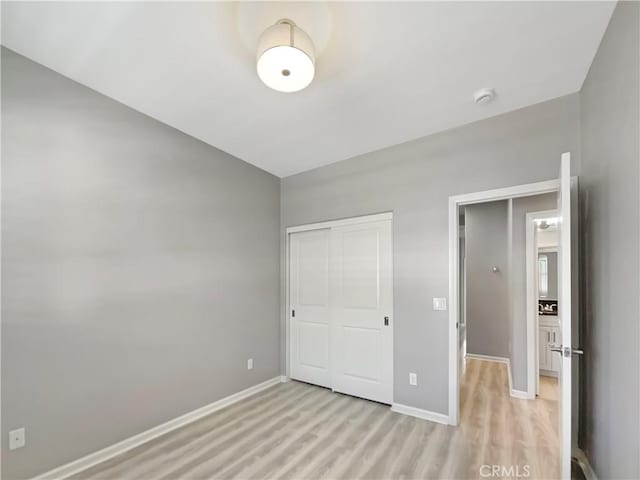 unfurnished bedroom featuring a closet, baseboards, and light wood-style floors