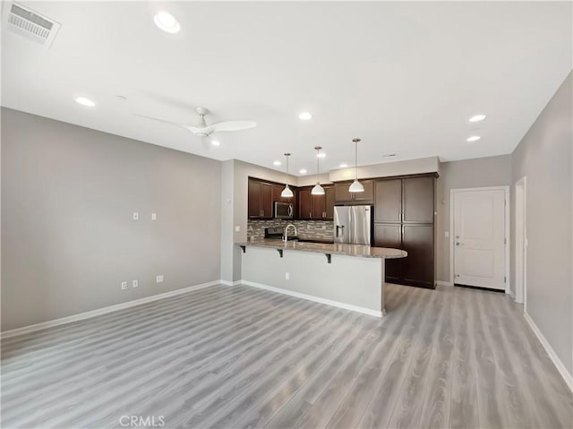 kitchen featuring visible vents, a peninsula, stainless steel appliances, dark brown cabinets, and a kitchen breakfast bar