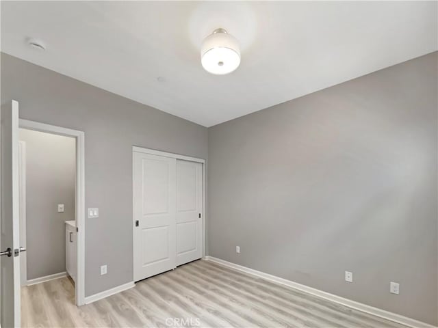 unfurnished bedroom featuring a closet, baseboards, and light wood-style floors