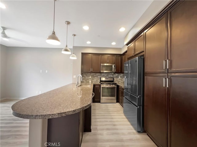 kitchen featuring light wood-style flooring, appliances with stainless steel finishes, a peninsula, decorative backsplash, and dark brown cabinets