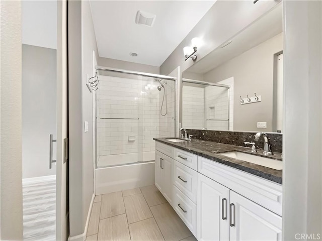 full bath with a sink, bath / shower combo with glass door, and double vanity