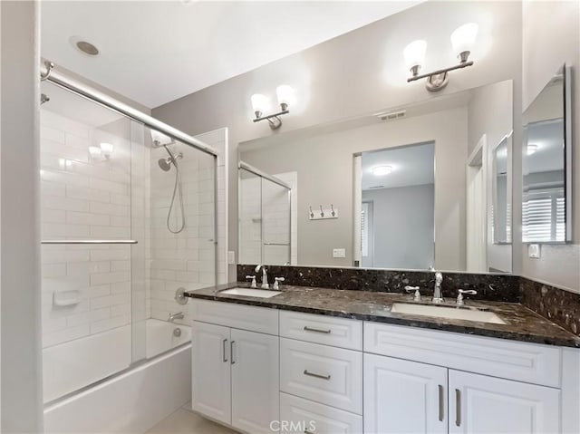 bathroom with double vanity, enclosed tub / shower combo, visible vents, and a sink