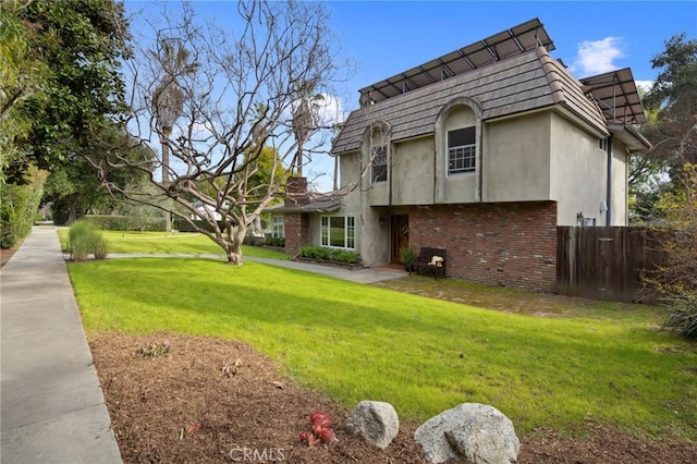 view of home's exterior featuring stucco siding, a lawn, mansard roof, fence, and brick siding