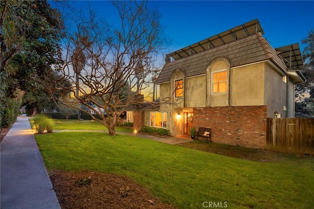 view of front facade featuring stucco siding, a front lawn, mansard roof, fence, and brick siding