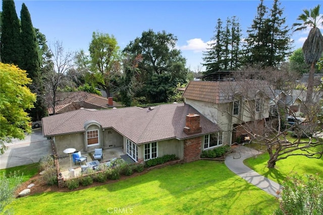 view of front of house featuring stucco siding, a patio, a chimney, and a front yard