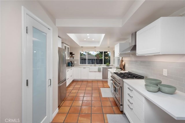 kitchen featuring wall chimney range hood, stainless steel appliances, light countertops, decorative backsplash, and a raised ceiling