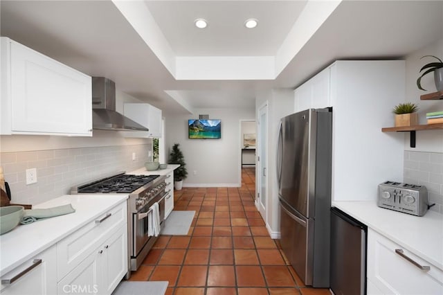 kitchen featuring white cabinetry, a raised ceiling, wall chimney exhaust hood, and appliances with stainless steel finishes