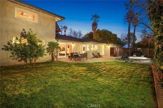 rear view of property with fence, a yard, stucco siding, a jacuzzi, and a patio area