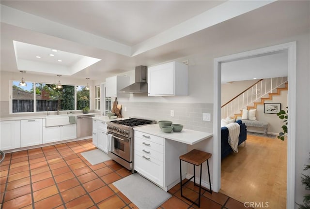 kitchen with a raised ceiling, white cabinets, wall chimney exhaust hood, and appliances with stainless steel finishes