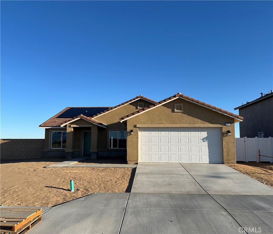 ranch-style home with fence, a tiled roof, concrete driveway, stucco siding, and an attached garage