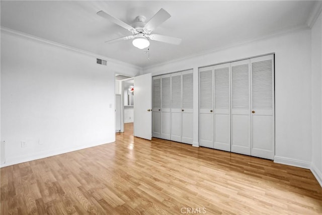 unfurnished bedroom with visible vents, two closets, crown molding, and light wood-style floors