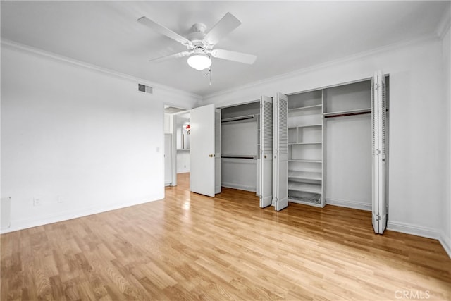 unfurnished bedroom with visible vents, baseboards, multiple closets, ornamental molding, and wood finished floors