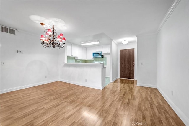 unfurnished living room featuring baseboards, visible vents, light wood finished floors, crown molding, and a notable chandelier