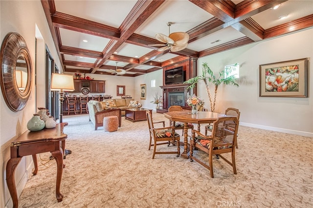 dining area featuring a ceiling fan, beam ceiling, light colored carpet, and a large fireplace