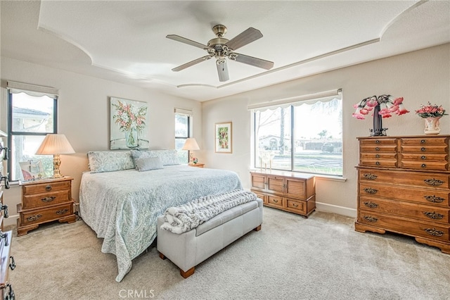 bedroom featuring light colored carpet, baseboards, a tray ceiling, and multiple windows