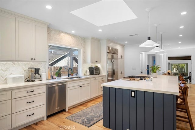 kitchen with a breakfast bar, a sink, light wood-style floors, appliances with stainless steel finishes, and a skylight