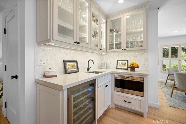 bar with tasteful backsplash, baseboards, beverage cooler, light wood-style floors, and a sink