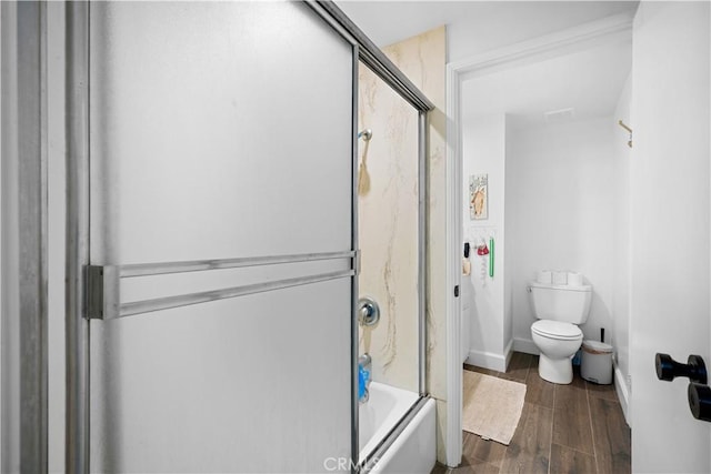 bathroom featuring toilet, wood finished floors, and combined bath / shower with glass door