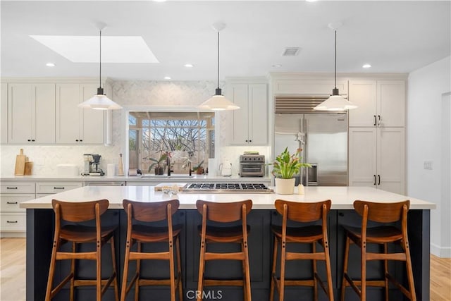 kitchen with visible vents, a kitchen island, decorative backsplash, light wood-style flooring, and appliances with stainless steel finishes