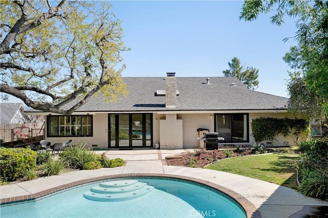 rear view of house with an outdoor pool, brick siding, a chimney, and fence