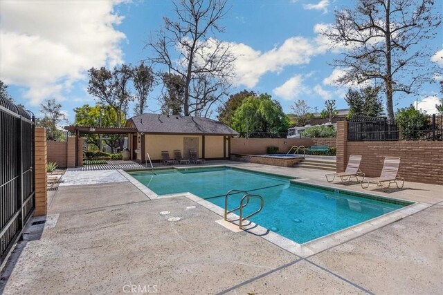 community pool featuring fence, a hot tub, and a patio area