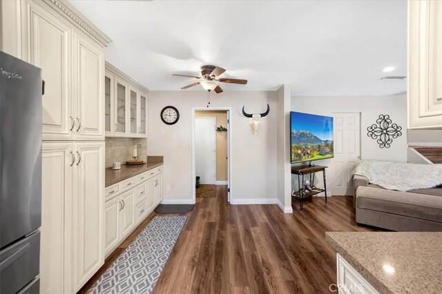 kitchen with dark wood-type flooring, decorative backsplash, freestanding refrigerator, glass insert cabinets, and ceiling fan