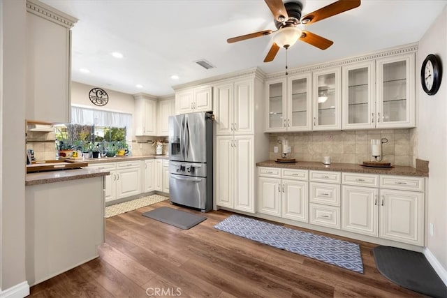 kitchen featuring tasteful backsplash, visible vents, glass insert cabinets, wood finished floors, and stainless steel fridge