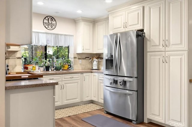 kitchen featuring backsplash, light stone countertops, light wood-type flooring, stainless steel fridge, and a sink