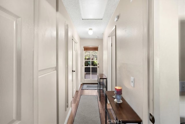 corridor with a textured ceiling and wood finished floors