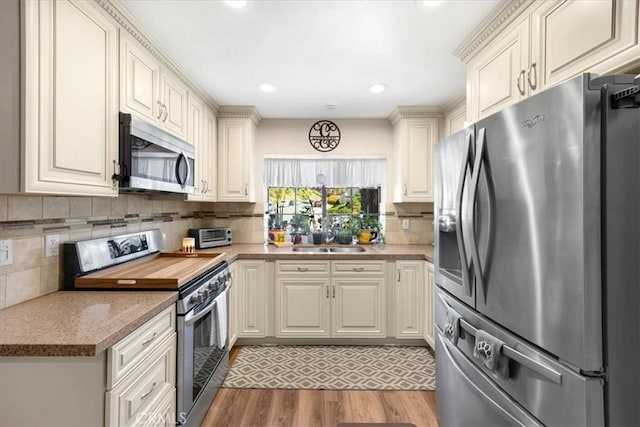 kitchen with light wood-type flooring, a sink, tasteful backsplash, stainless steel appliances, and light countertops