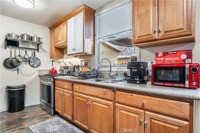 kitchen with dark wood-type flooring, a sink, gas stove, brown cabinetry, and baseboards