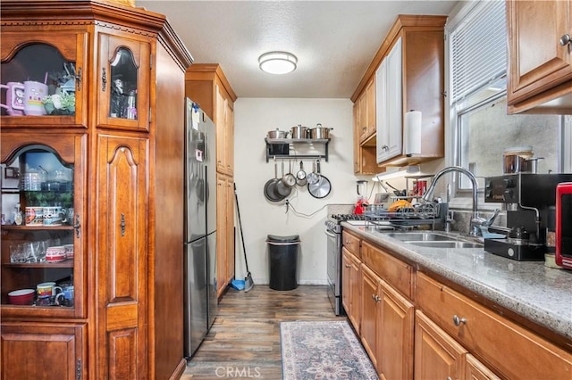 kitchen featuring brown cabinets, a sink, wood finished floors, appliances with stainless steel finishes, and baseboards