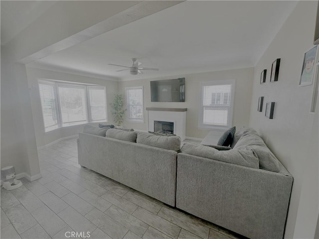 living room featuring a ceiling fan, a fireplace, baseboards, and ornamental molding