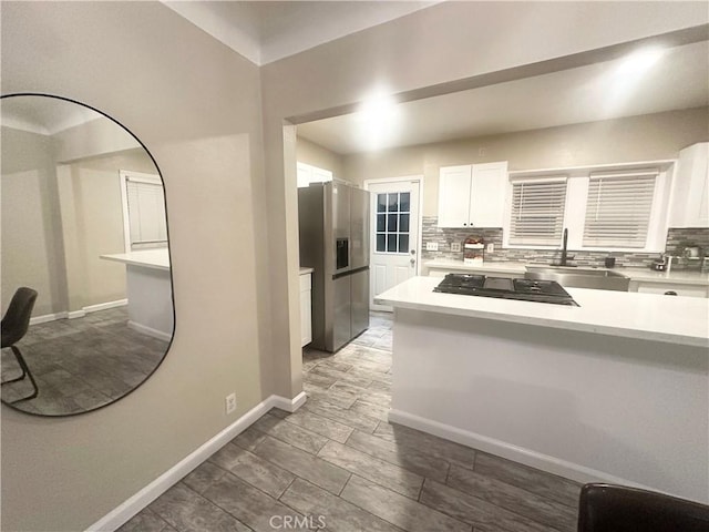 kitchen featuring stainless steel fridge with ice dispenser, light countertops, decorative backsplash, white cabinetry, and a sink