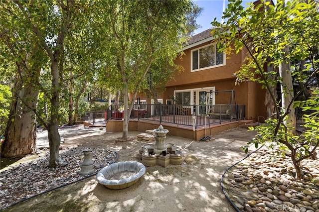 rear view of house featuring stucco siding, a wooden deck, and a patio area