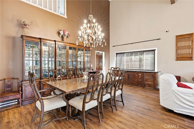 dining area with a wealth of natural light, an inviting chandelier, wood finished floors, and a towering ceiling