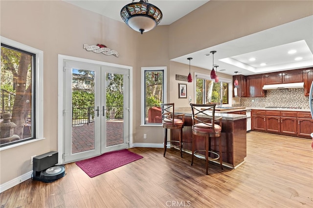 kitchen featuring a breakfast bar area, a peninsula, french doors, light wood-style floors, and under cabinet range hood