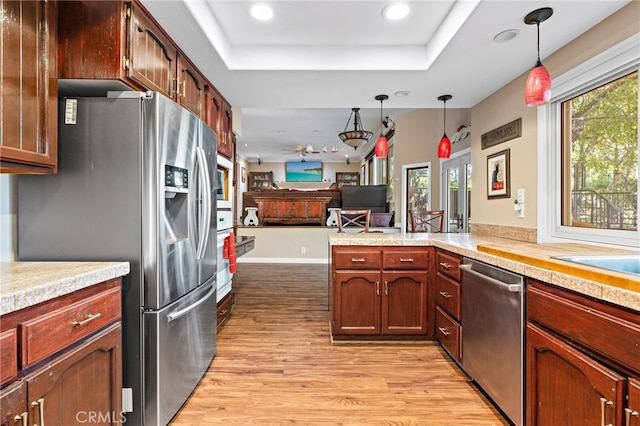 kitchen featuring a raised ceiling, decorative light fixtures, open floor plan, and stainless steel appliances