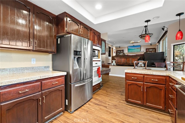 kitchen with light wood finished floors, a tray ceiling, stainless steel appliances, hanging light fixtures, and light countertops