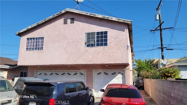 view of front facade featuring stucco siding, a garage, and fence