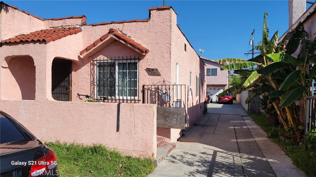 view of side of property with stucco siding, fence, and a tiled roof