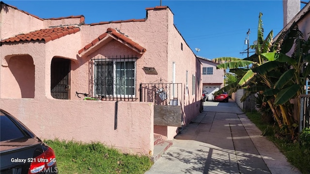 view of side of property with stucco siding, fence, and a tiled roof