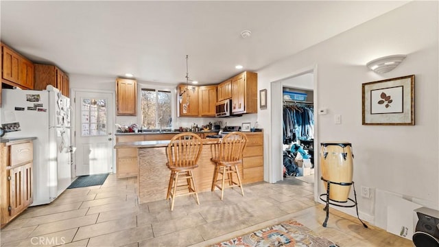 kitchen featuring stainless steel microwave, freestanding refrigerator, recessed lighting, a breakfast bar area, and range